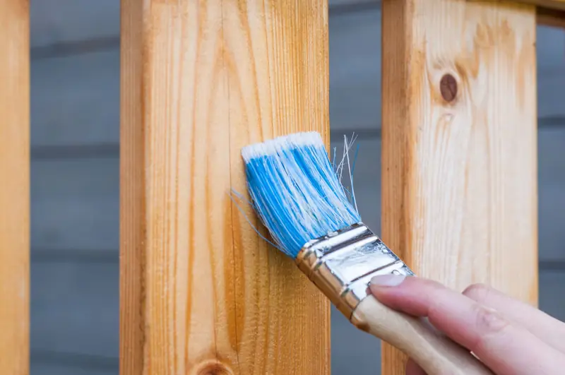Brush applying paint to a wooden fence