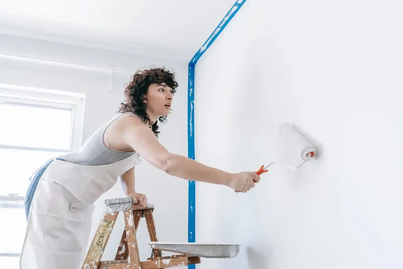 Painter on a ladder painting an interior wall white